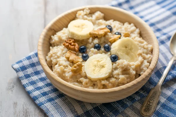 Oatmeal with bananas and blueberries in a wooden bowl — Stock Photo, Image