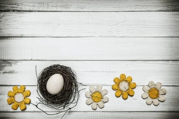 Huevo en nido con flores alrededor sobre fondo de madera — Foto de Stock