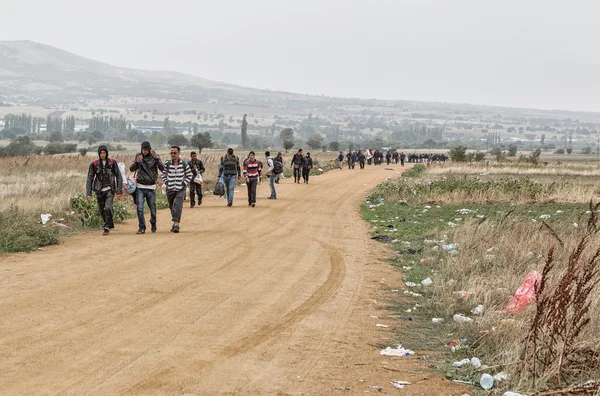 Refugiados e migrantes que caminham pela estrada empoeirada — Fotografia de Stock