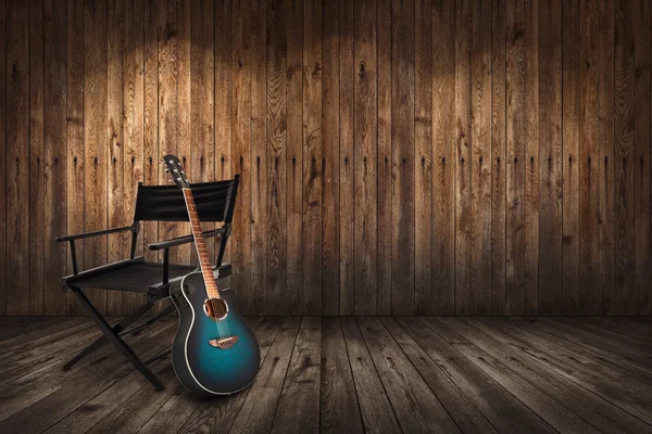 Guitar near chair on wooden wall background — Stock Photo, Image