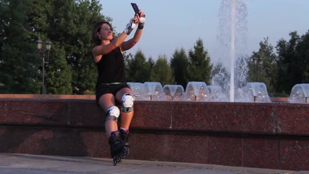 Menina com equipamento de lâminas de rolo tirando fotos no celular no parque — Vídeo de Stock