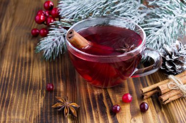 Sıcak çaya yakın çekim, ahşap arka plandaki cam fincanda kızılcık ve baharatlar var.