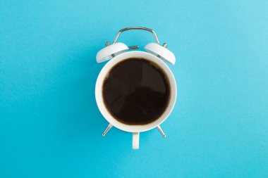 Kahvenin üst görüntüsü mavi arkaplanın ortasındaki beyaz çalar saatin kadranında.