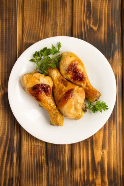 Ahşap arka plandaki beyaz tabakta kızarmış tavuk bacağı manzarası. Konum dikey.