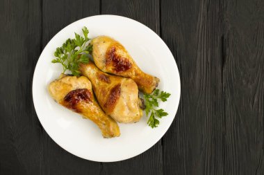 Siyah ahşap arka planda beyaz tabakta kızarmış tavuk bacağı manzarası.