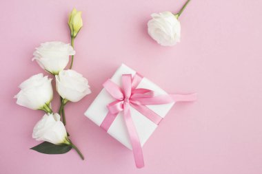 Hediye kutusunun üst görüntüsü, pembe arka planda beyaz ve pembe çiçekler.