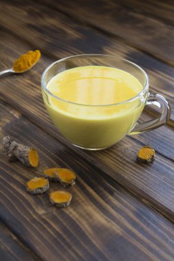 Tahta arka plandaki beyaz bardakta zerdeçal içeren altın süt.