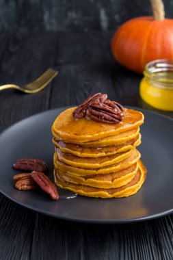 Ballı ev yapımı balkabağı krepleri ve siyah arka planda fındıklar.