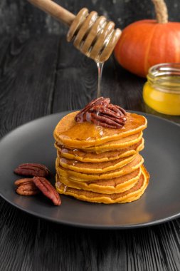 Ballı ev yapımı balkabağı krepleri ve siyah arka planda fındıklar.