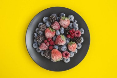 Sarı arkaplandaki siyah tabakta donmuş böğürtlenlerin üst görüntüsü