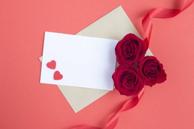 Metin için boş beyaz kağıdın üst görünümü, kırmızı yüzeyde kırmızı güller ve kalpler