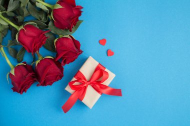 Kırmızı güllerin üst görüntüsü, mavi arka planda hediyeler ve kalpler.