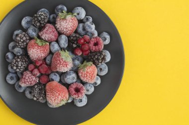 Sarı yüzeydeki siyah tabakta donmuş böğürtlenlere yaklaş.