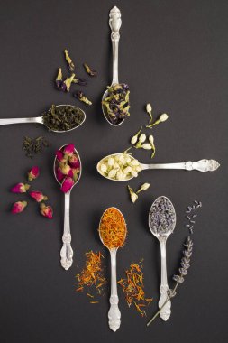 Siyah yüzeydeki gümüş kaşıklarda farklı çay çeşitlerinin üst görünümü