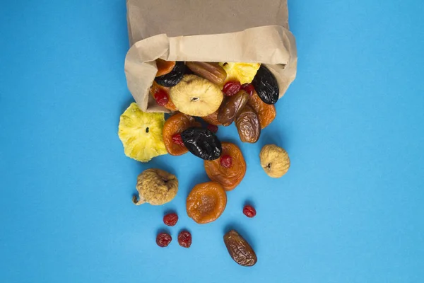 Top view of different dried fruits in a paper bag on the blue background