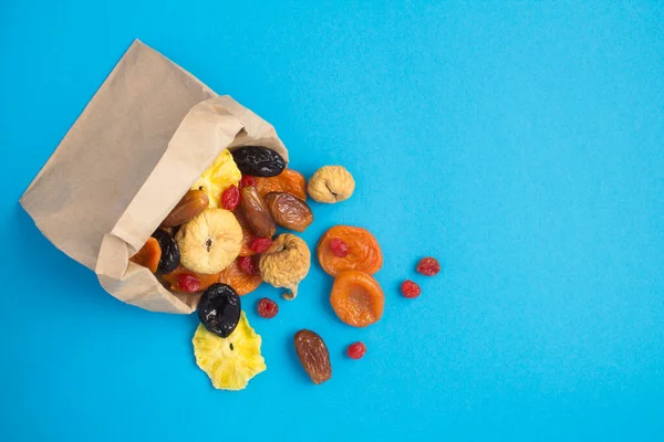 Top view of different dried fruits in a paper bag on the blue background