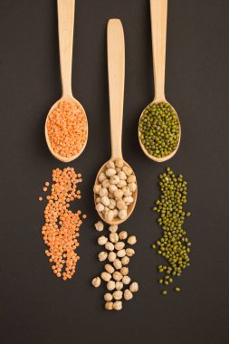 Kırmızı mercimek, nohut ve koyu yüzeydeki tahta kaşıklarda ezme manzarası. Konum dikey.