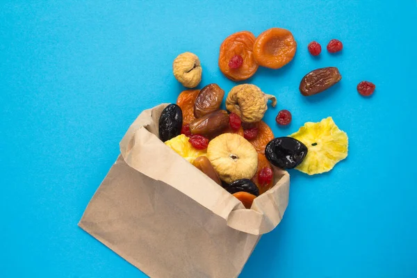 Top view of different dried fruits in a paper bag on the blue background