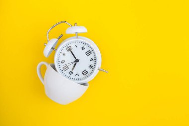 Beyaz alarm saati ve sarı arka planda beyaz bardak.