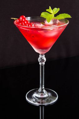 Siyah arka plandaki martini bardağında kırmızı üzümlü soğuk kokteyl. Konum dikey.