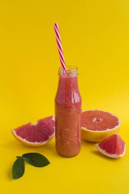 Sarı arka planda cam bir şişede greyfurtlu smoothie. Yakın plan. Konum dikey.