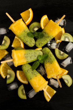 Siyah ahşap arka planda kivi ve portakal meyveli buzlu dondurma manzarası. Konum dikey.