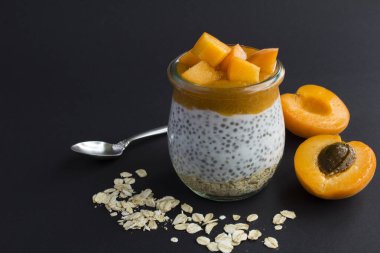 Puding, chia tohumu, yulaf gevreği ve siyah arka plandaki cam kavanozda kayısı. Boşluğu kopyala.