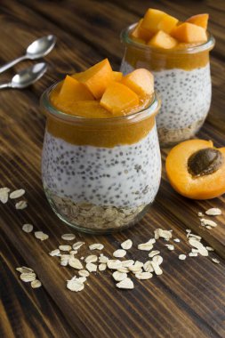 Chia tohumlu puding, yulaf ezmesi ve kayısı, ahşap masadaki cam kavanozlarda.