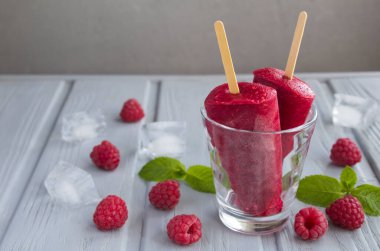 Buzlu şekerlere yakın plan, gri arka planda ahududulu içecek bardağı var.