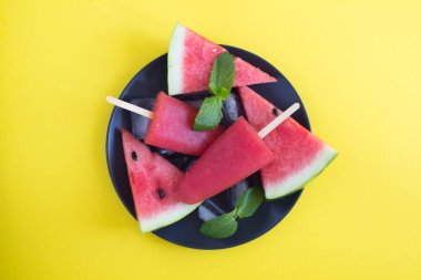 Sarı arka planda siyah tabakta karpuz olan buzlu şekerlerin üst görüntüsü. Yakın plan..