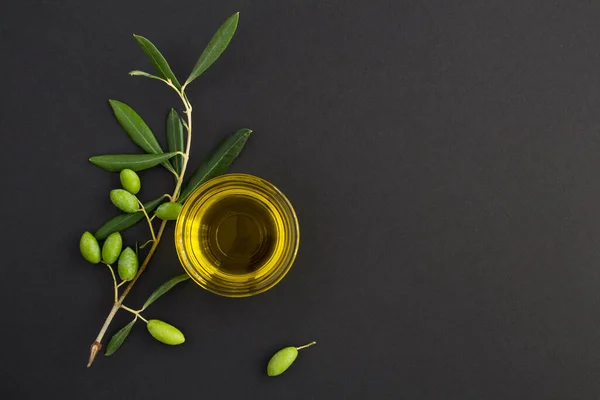 Cam bir kasede zeytinyağı ve siyah arka planda yeşil zeytin dalının üst görüntüsü. Boşluğu kopyala.