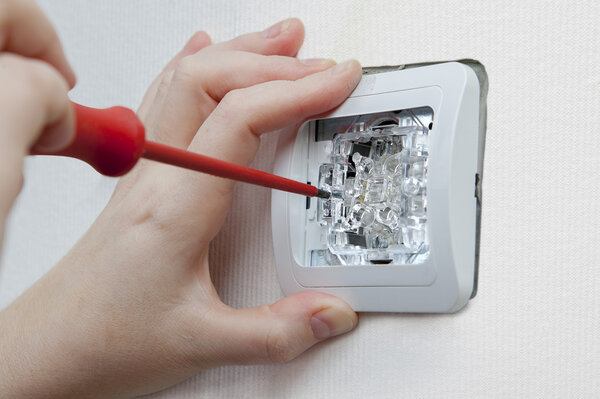 Wall mounting household light switch using screwdriver, electrician hand close-up.