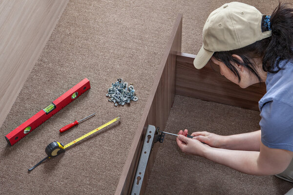 Woman assembles furniture, hinges lifting mechanism screwed to bed frame.