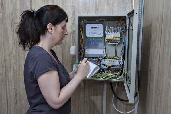 Mujer revisando mostrador eléctrico, de pie cerca de equipos de distribución de electricidad en el interior . — Foto de Stock