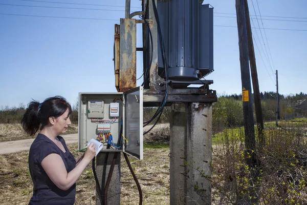 Mujer revisando lectura de contador eléctrico, de pie cerca de la subestación del transformador de potencia . — Foto de Stock