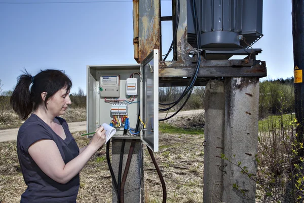 Villanyszerelő mérnök nő ellenőrzési villamosenergia mérővel és a számla, a szabadban alállomás. — Stock Fotó