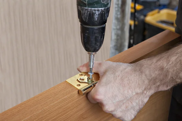 Installeren van deur scharnieren, timmerman aanscherping schroeven met behulp van de schroevendraaier bits boor. — Stockfoto