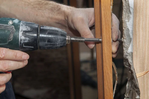 Carpenter fix jamb in doorway using a cordless drill electric screwdriver, close-up. — Stock Photo, Image