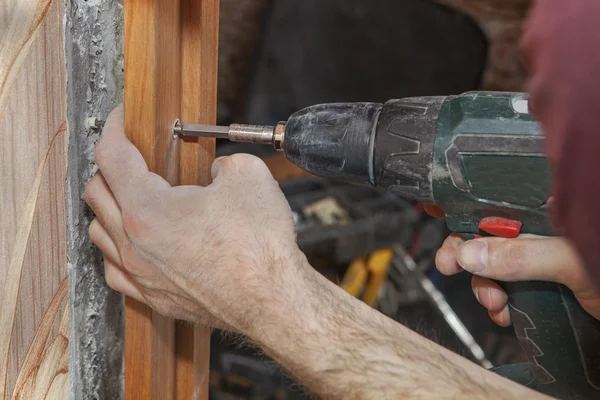 Woodworker wkręca ościeżnicy w drzwiach przy użyciu akumulatorowa wiertarko-wkrętarka elektryczna. — Zdjęcie stockowe