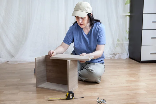 Ein kaukasisches Mädchen montiert neue Möbel, während es auf dem Boden sitzt. — Stockfoto