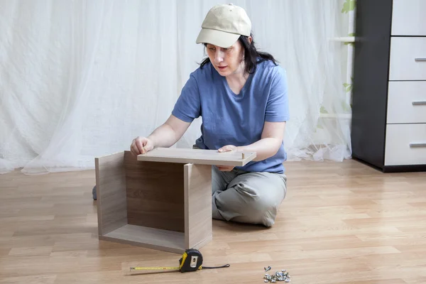 One Caucasian girl mounts new furniture while sitting on floor. — Stock Image One Caucasian girl mounts new furniture while sitting on floor. Stock Image