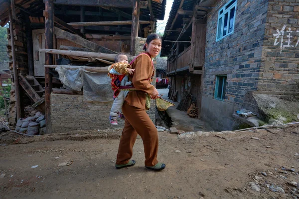 Asian kobieta idzie na ulicy wiejskiej, noszenia dziecka na plecach. — Zdjęcie stockowe