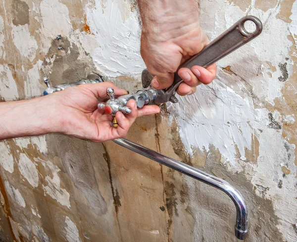 Hands plumber with an adjustable wrench, nut unscrewed flowing tap. — Stock Photo, Image