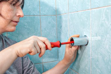 Woman with screwdriver, tighten screw bracket for shower to wall. clipart
