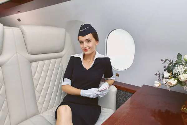 Air hostess inside airplane sits near porthole.