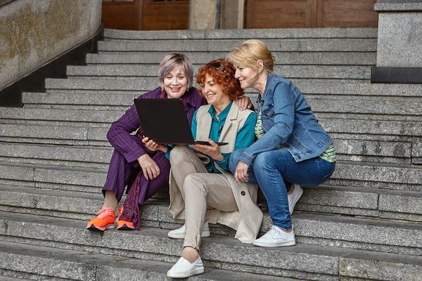 Mulheres idosas felizes com laptop sentar-se nas escadas. — Fotografia de Stock