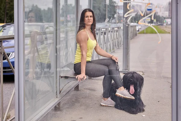 Vrouwelijke en zwarte hond wachten op bus. — Stockfoto