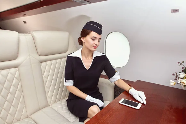 Stewardess sitzt mit Handy in der Business Class des Flugzeugs. — Stockfoto