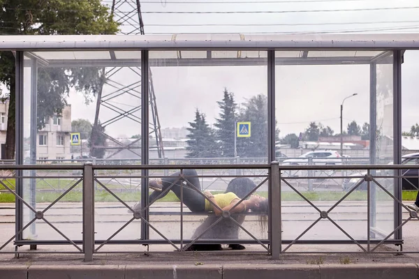 Женщина с бриардом лежит на скамейке остановки общественного транспорта. — стоковое фото