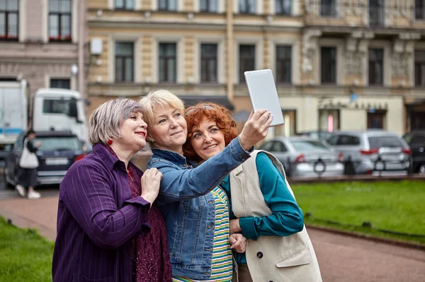 Cheerful pretty middle-aged women take selfie on tablet PC.